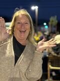 Smiling person in a sparkly gold jacket claps at an outdoor event at night.