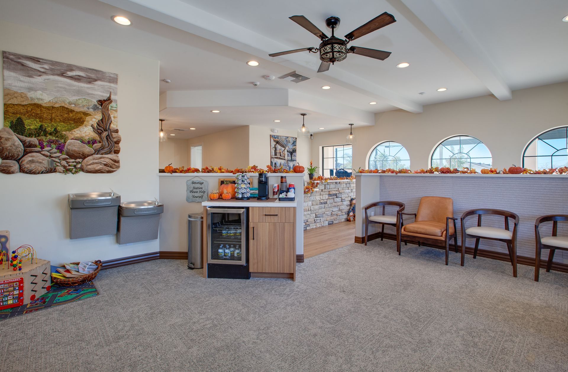 Bright lobby lounge with bar counter, chairs, ceiling fan, and carpeted floor