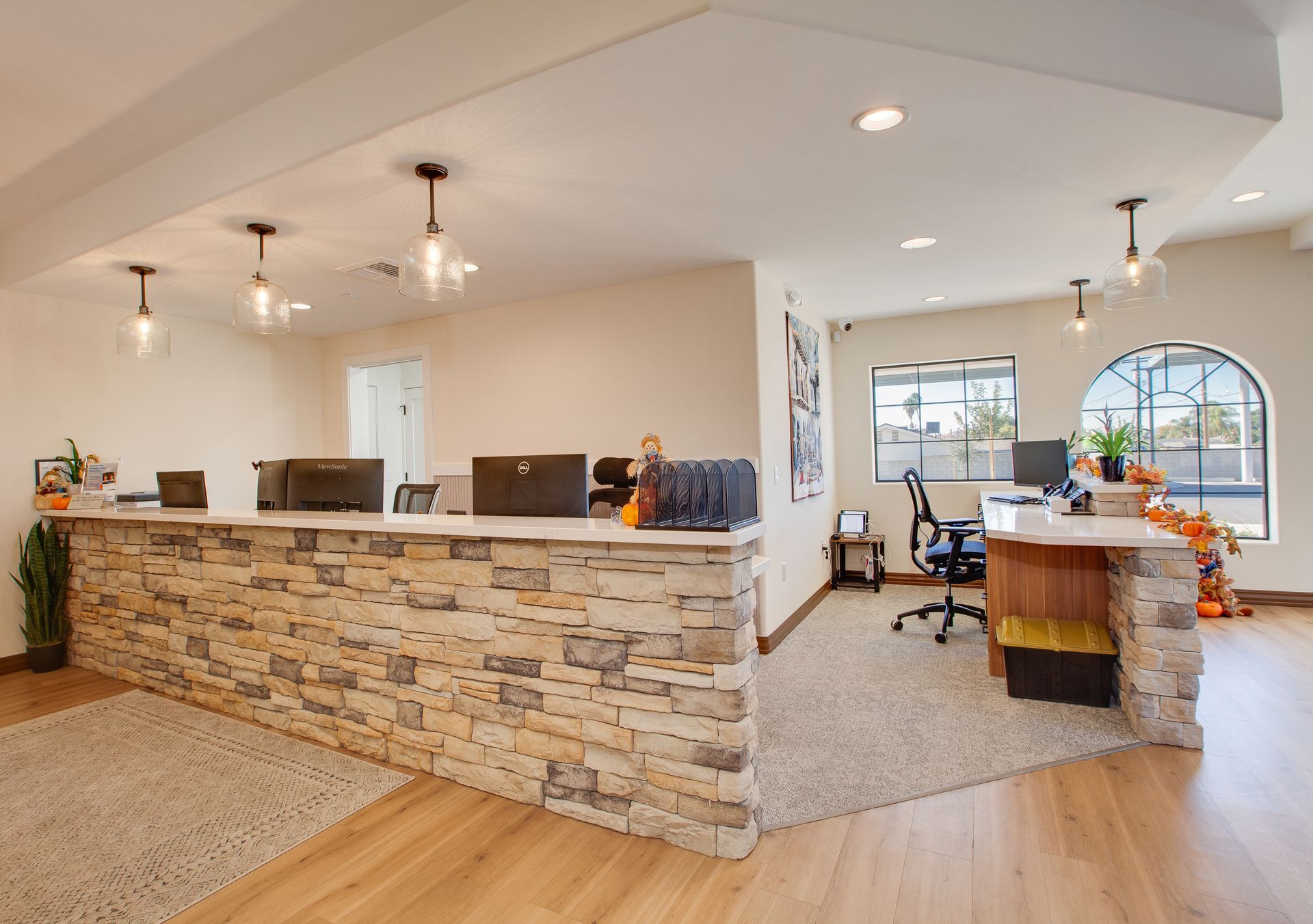 Bright reception area with stone-front desk, white walls, wood floors, and office chairs near windows