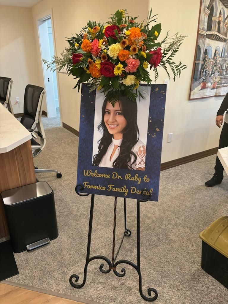 Memorial photo display with colorful flowers and a tribute sign on a wrought-iron stand indoors