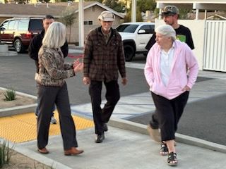 Three people walking together on a sidewalk near parked cars and houses