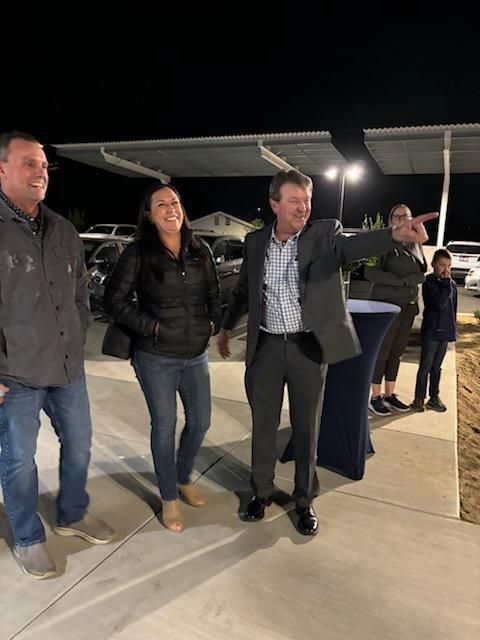 Four people standing outside at night under bright lights, one pointing ahead near a covered seating area.