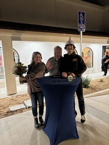 Three people standing beside a blue cocktail table at night, with a building and handicap parking sign behind them
