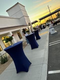 Blue cocktail tables on a sidewalk outside a white building at sunset.