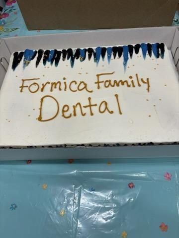 Handmade sign reading “Formica Family Dental” with blue and black fringe on top, on a light blue surface