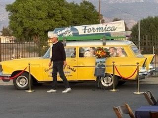 Yellow vintage car with a rooftop sign parked behind a roped barrier outdoors
