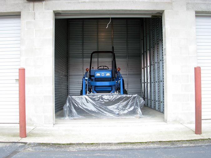 A blue tractor is parked in a garage with the door open.