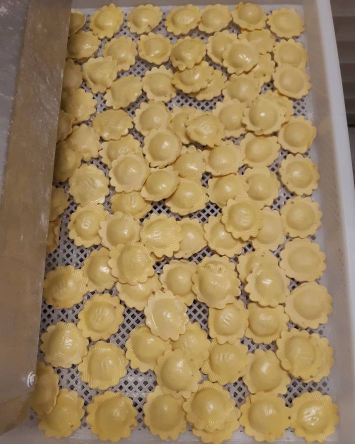 Un vassoio rettangolare pieno di numerosi ravioli crudi dai bordi ondulati, disposti su una superficie a rete.