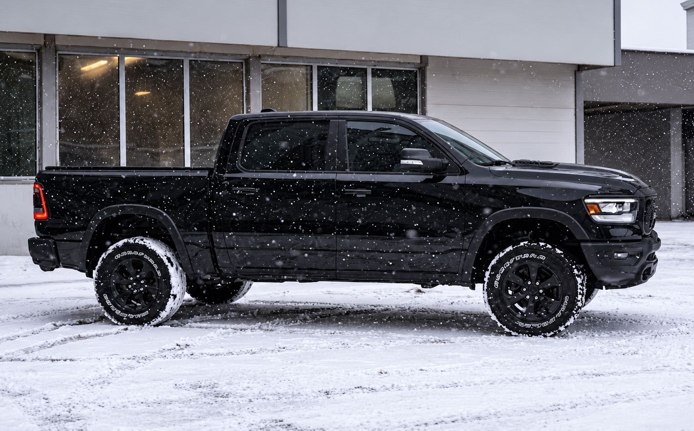 Black pickup truck parked in falling snow outside a building