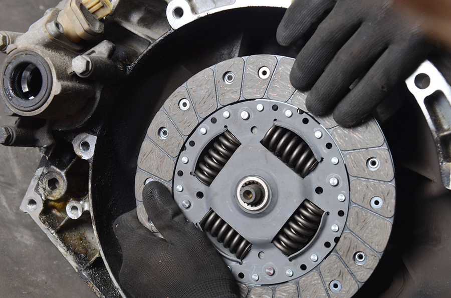 A person is holding a clutch plate on top of a car engine.