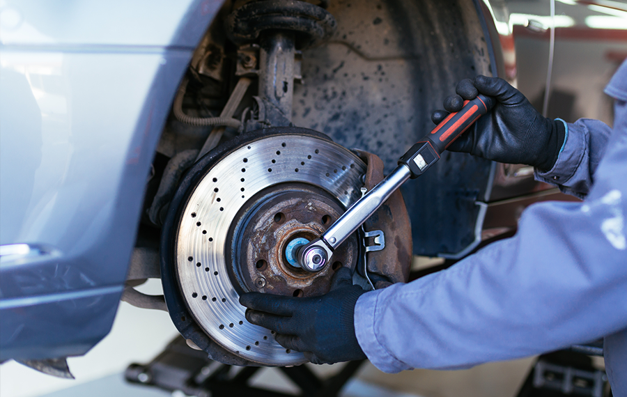 A man is working on the brake disc of a car with a wrench.