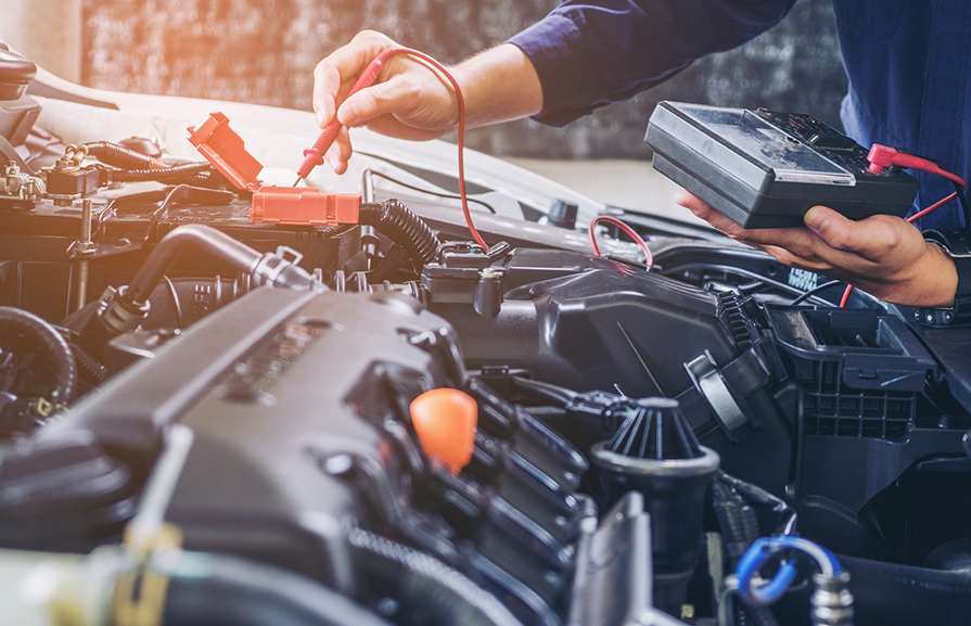 A mechanic is working on a car with a multimeter.