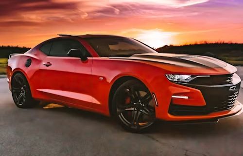 Red sports car parked on a road at sunset with a dramatic orange sky.