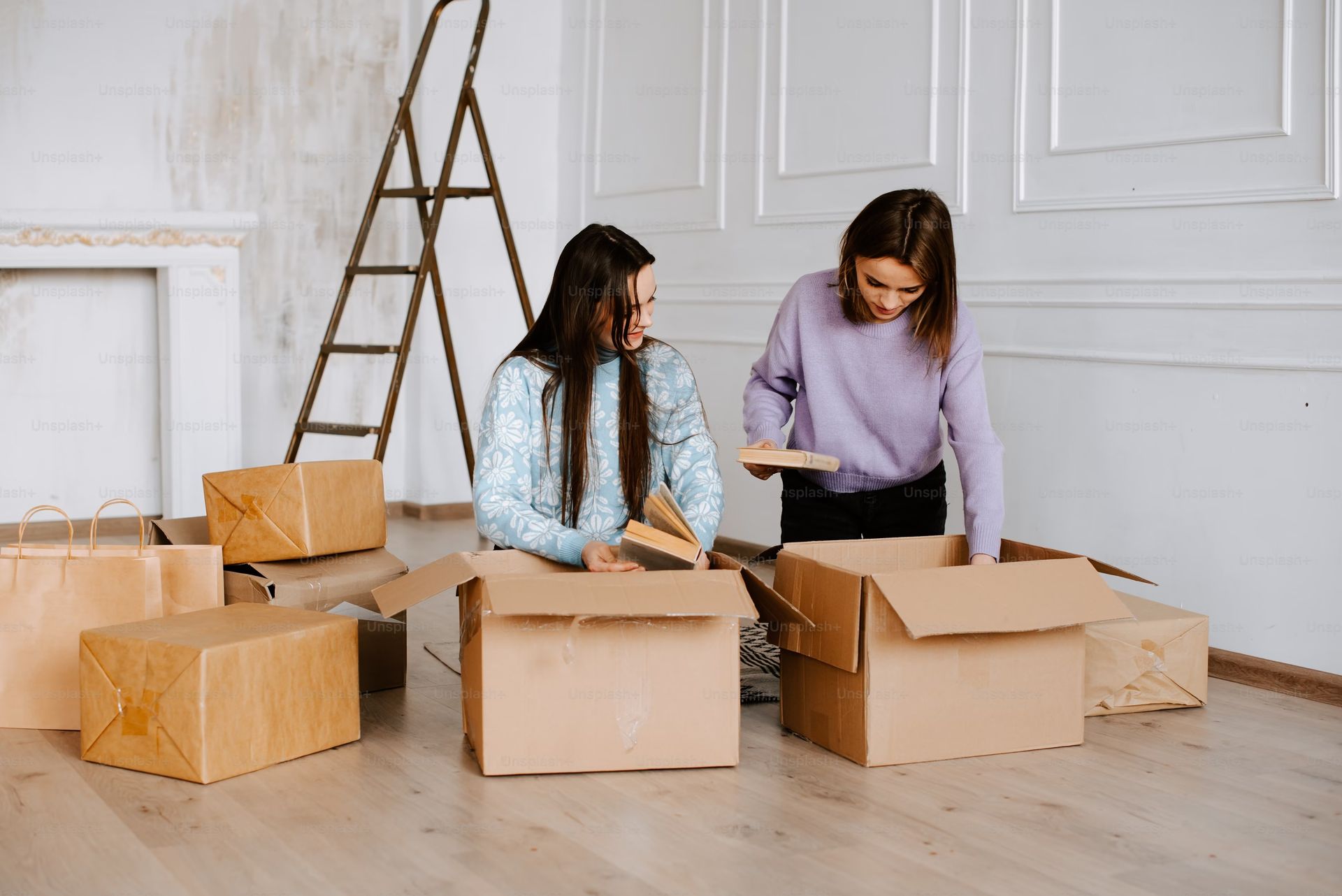 Two women carefully packing fragile items into cardboard boxes, preparing for storage at Gem Village Storage.