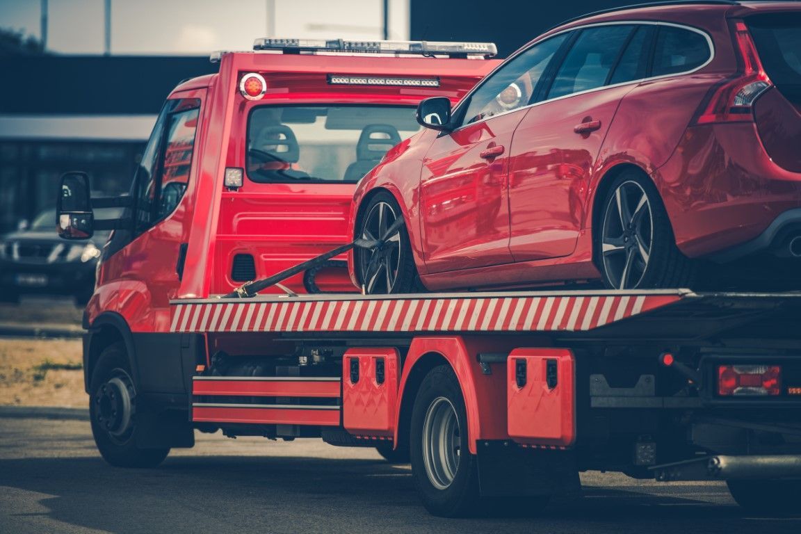 Red passenger vehicle being towed by flat bed tow truck