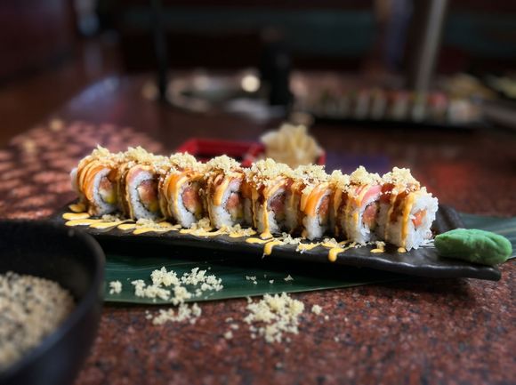 Sushi roll topped with sauce on a black plate, served on a restaurant table