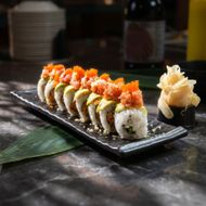 Sushi rolls topped with orange roe on a black plate, with pickled ginger on the side, on a dark table.