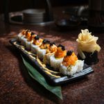 Sushi rolls topped with orange roe and black caviar on a black plate, with pickled ginger on the side