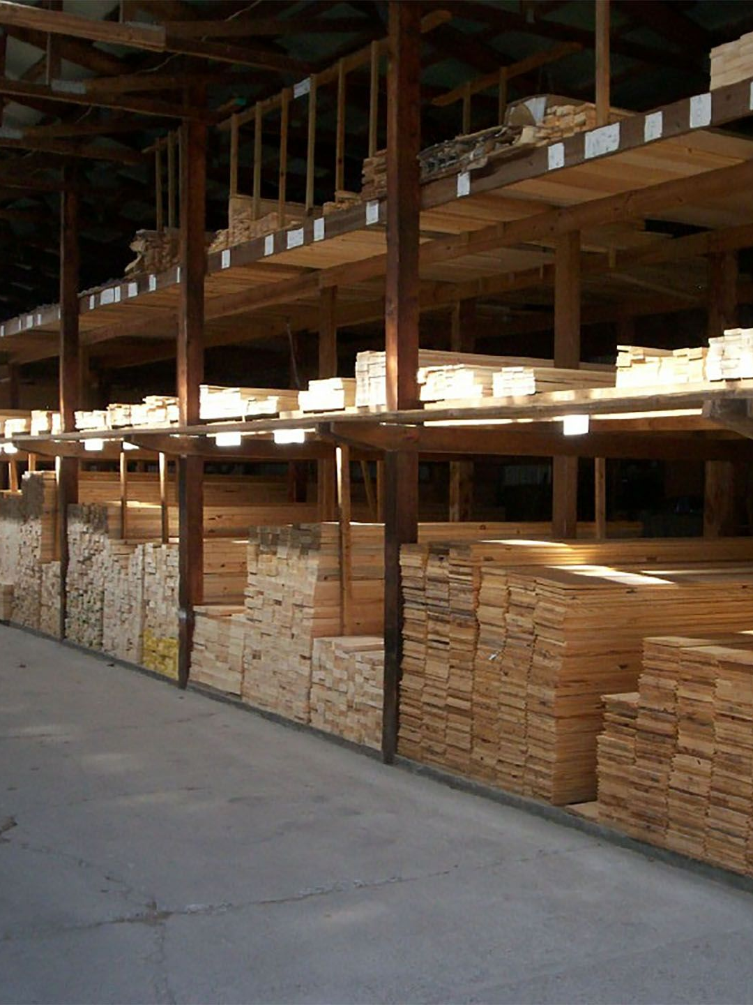 Stacks of lumber stored on wooden racks inside a warehouse with a concrete floor