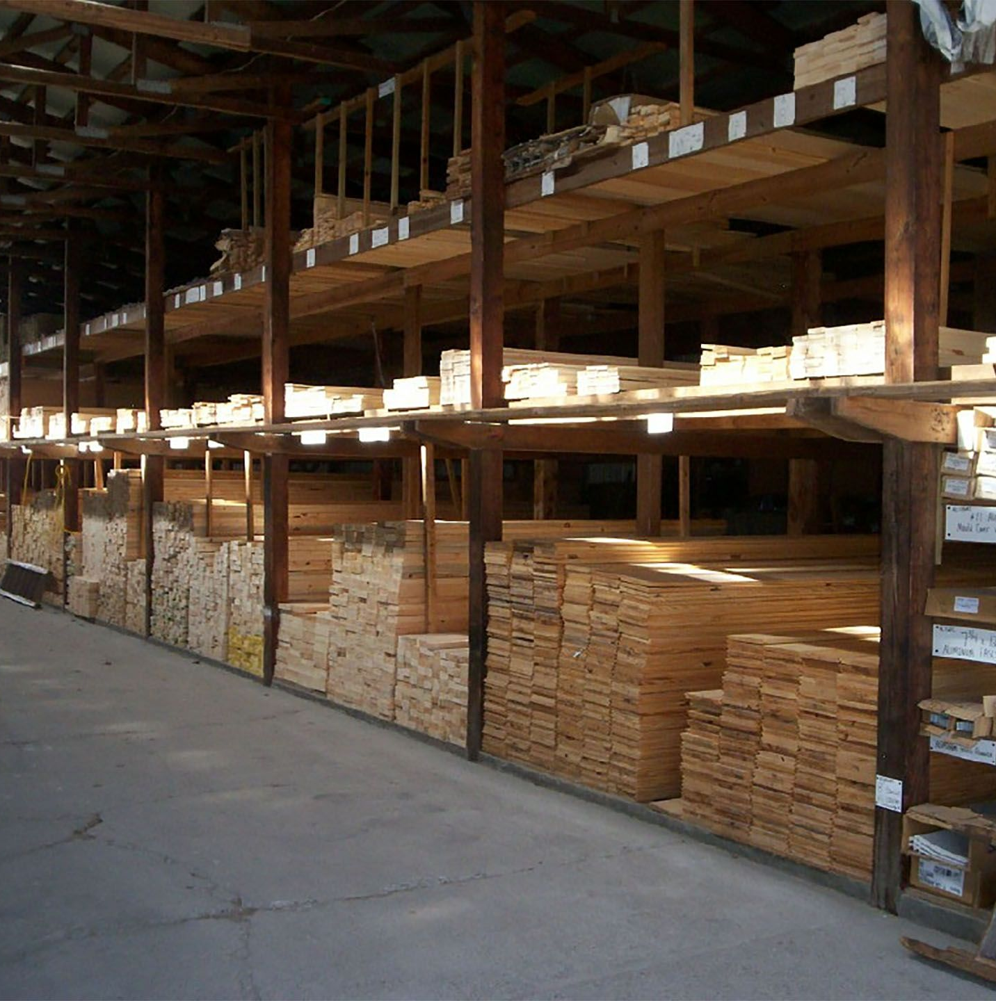 Wooden lumber stacks stored on industrial warehouse shelving along a concrete aisle.