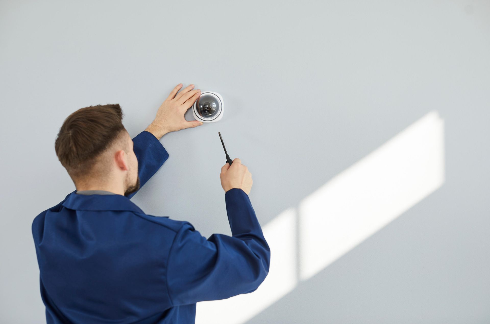 A man is installing a security camera on a wall.