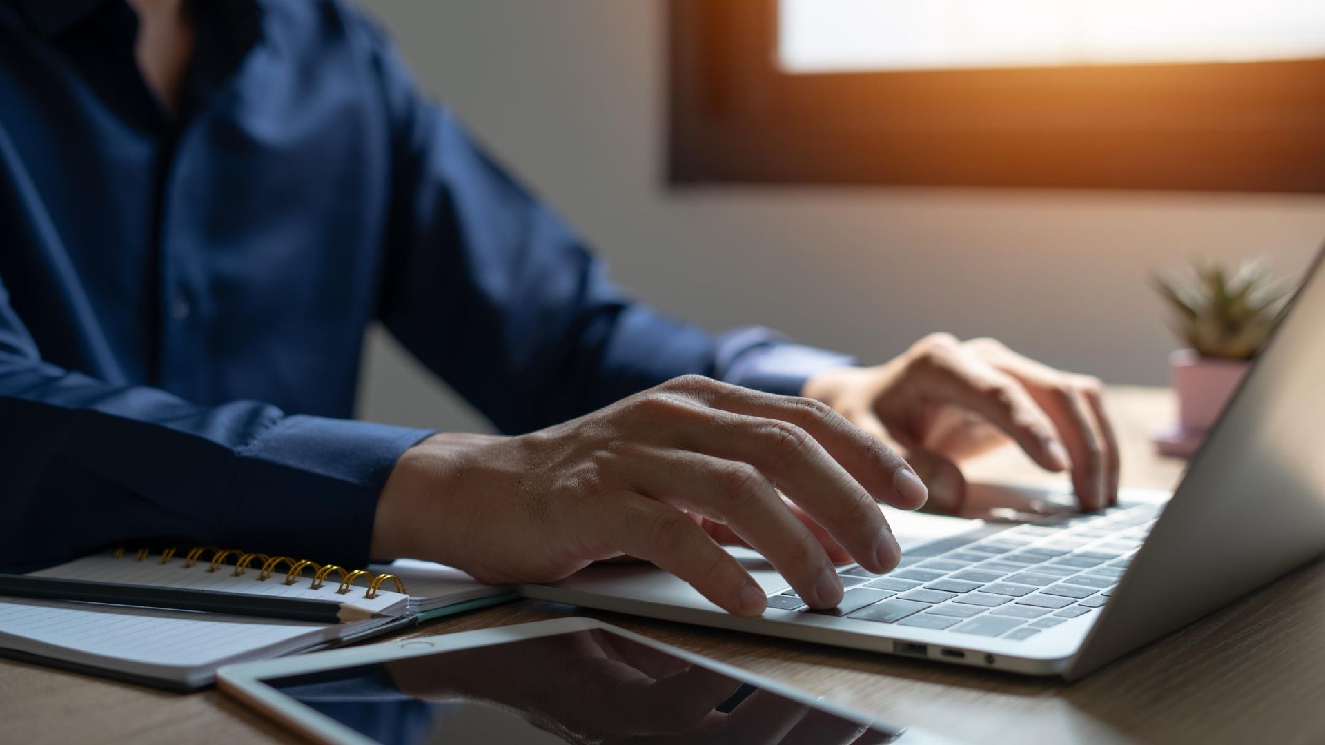 A man is typing on a laptop computer at a desk.