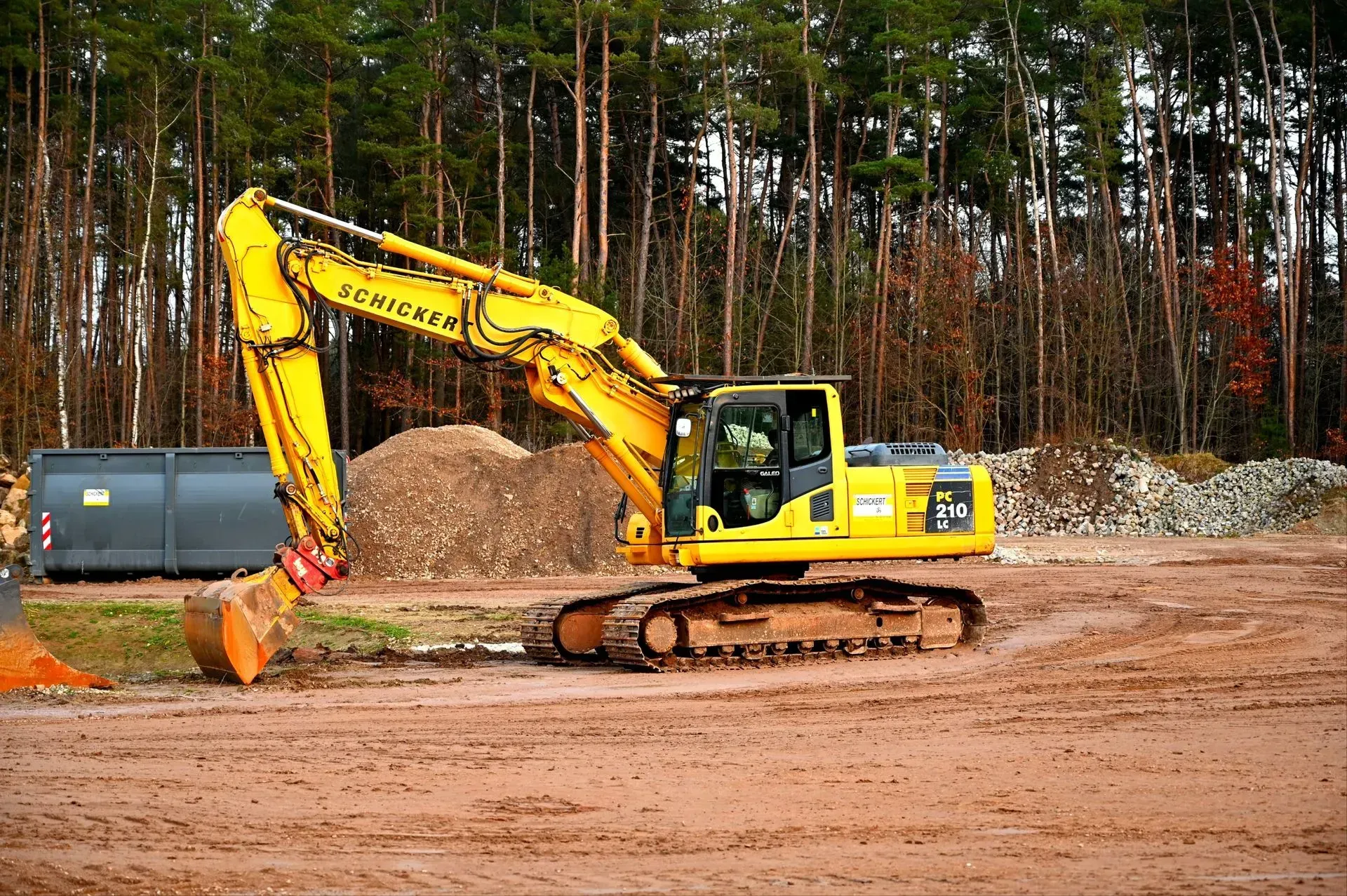 Yellow excavator loading dirt at a construction site with trees in the background