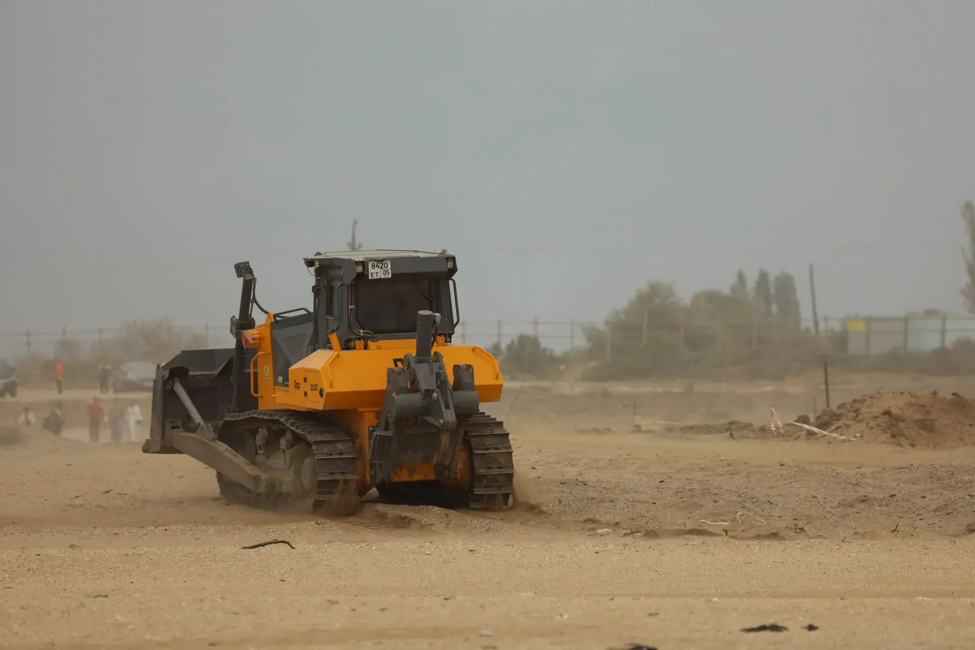 Yellow construction loader driving through a dusty road at a work site