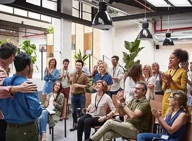 Team meeting in a bright office, with people sitting and standing while listening and clapping
