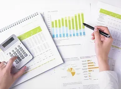 Calculator beside financial charts while a hand points at a bar graph on a desk