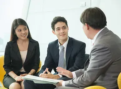 Three people in business attire discussing documents in a meeting room