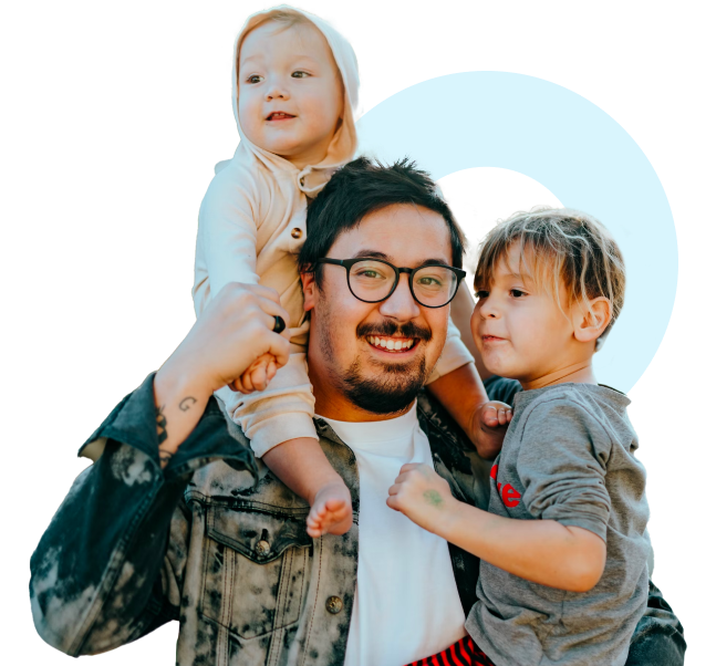 A smiling person wearing glasses holds a child on their shoulders while standing next to another child.