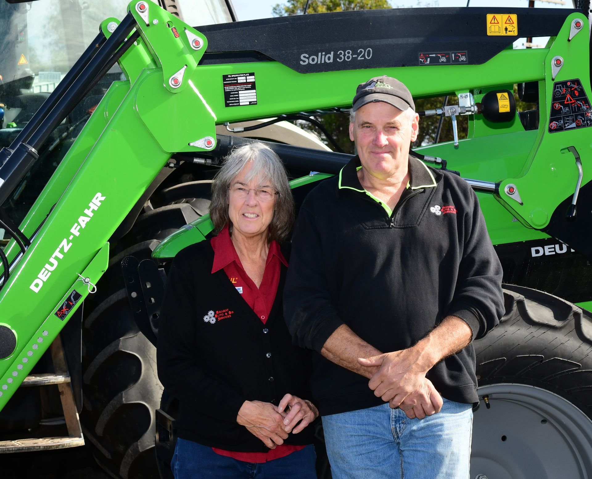Two people standing in front of a green Deutz-Fahr tractor, smiling outdoors