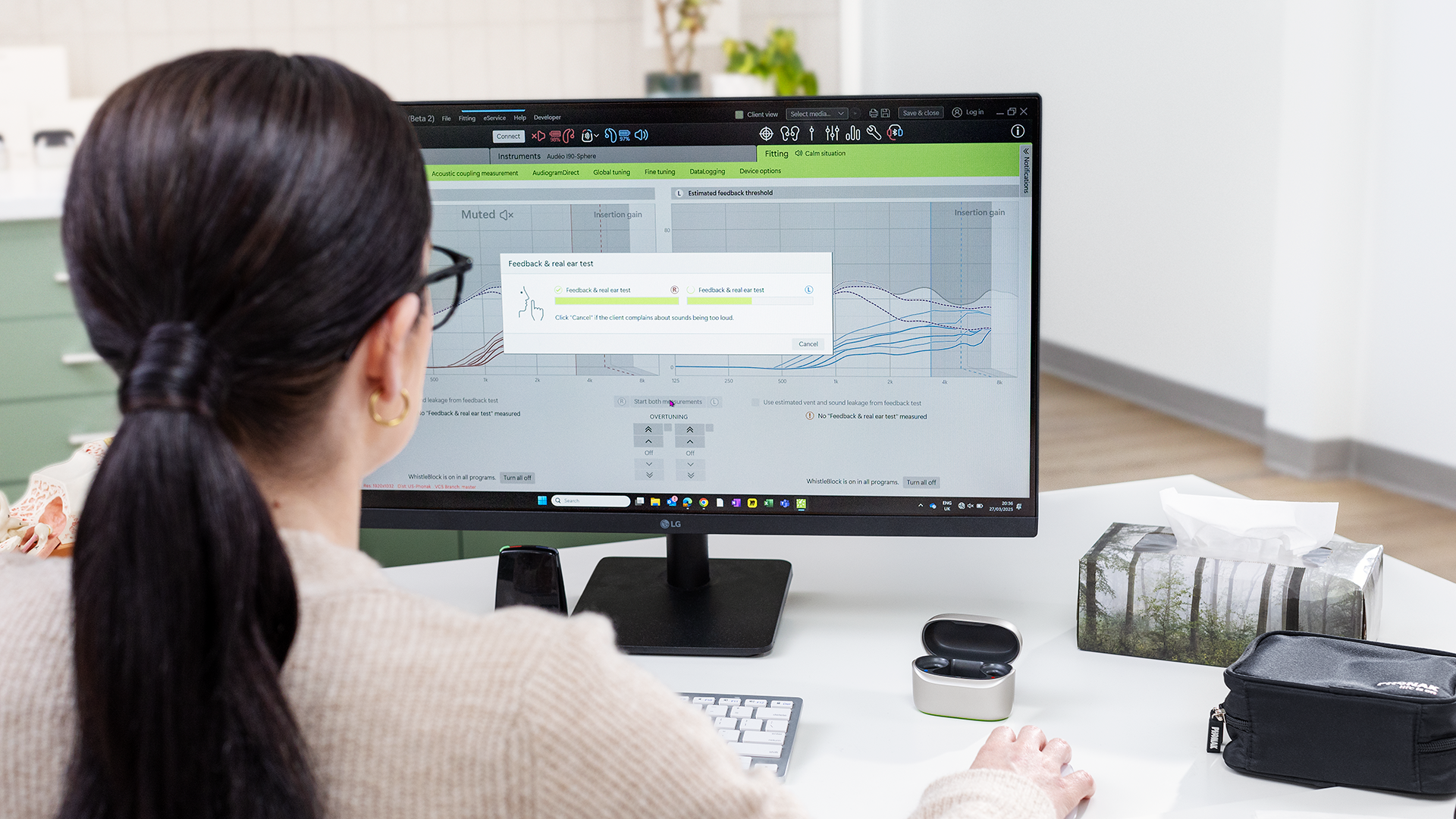 Person working at a desktop computer in a bright office, with a monitor displaying a software screen.