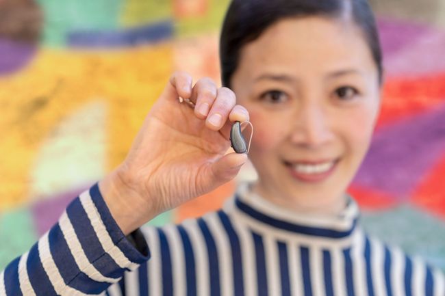 Woman holding up a small object in front of a colorful background, wearing a blue-and-white striped shirt