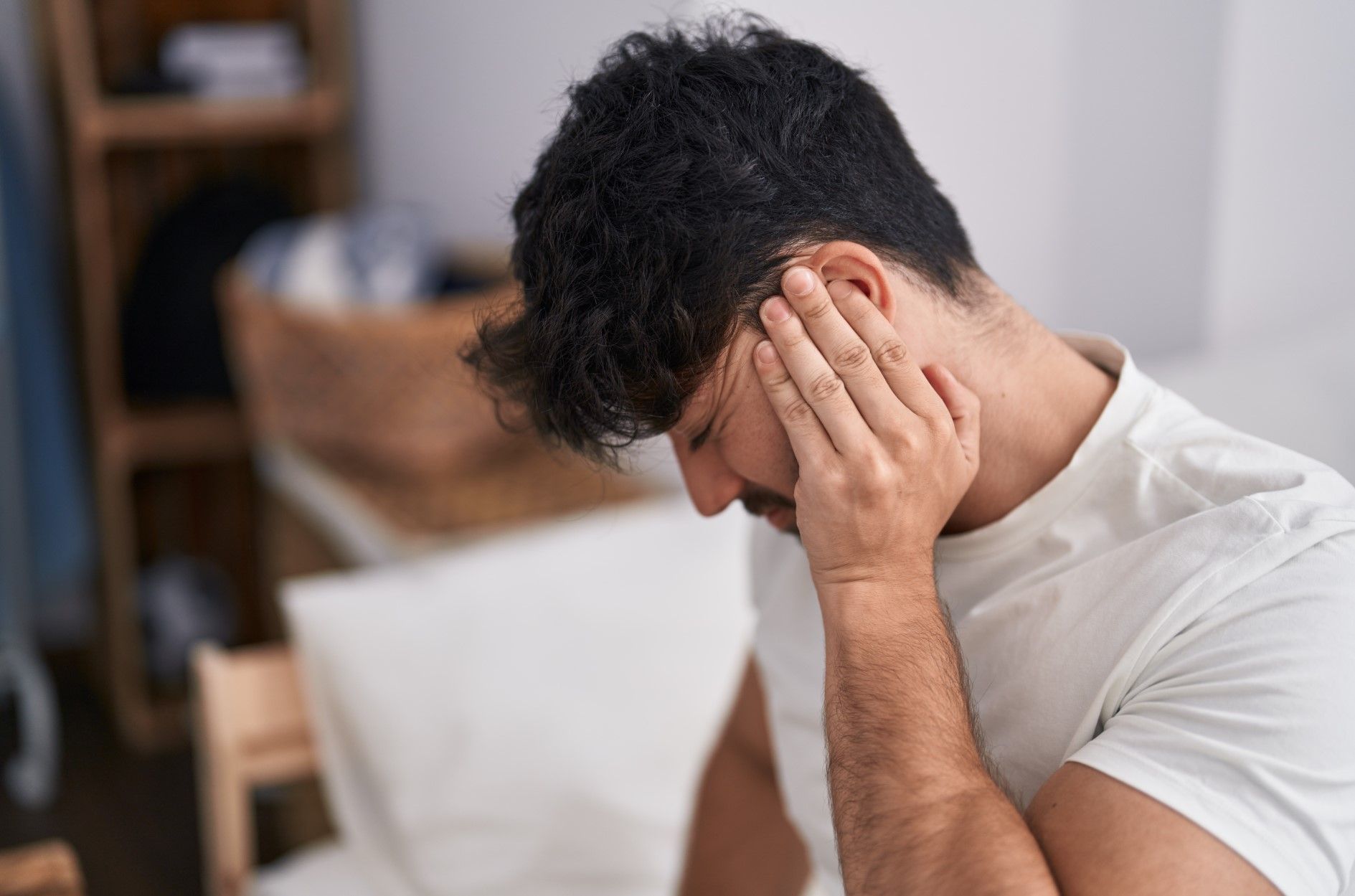 Person holding their head with eyes closed on a couch, appearing stressed or in pain.