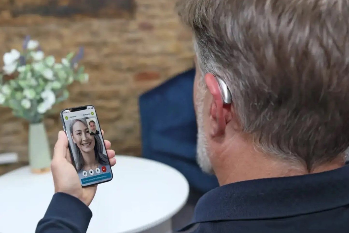 Man using a smartphone video call, viewing a smiling woman on the screen in a cozy room