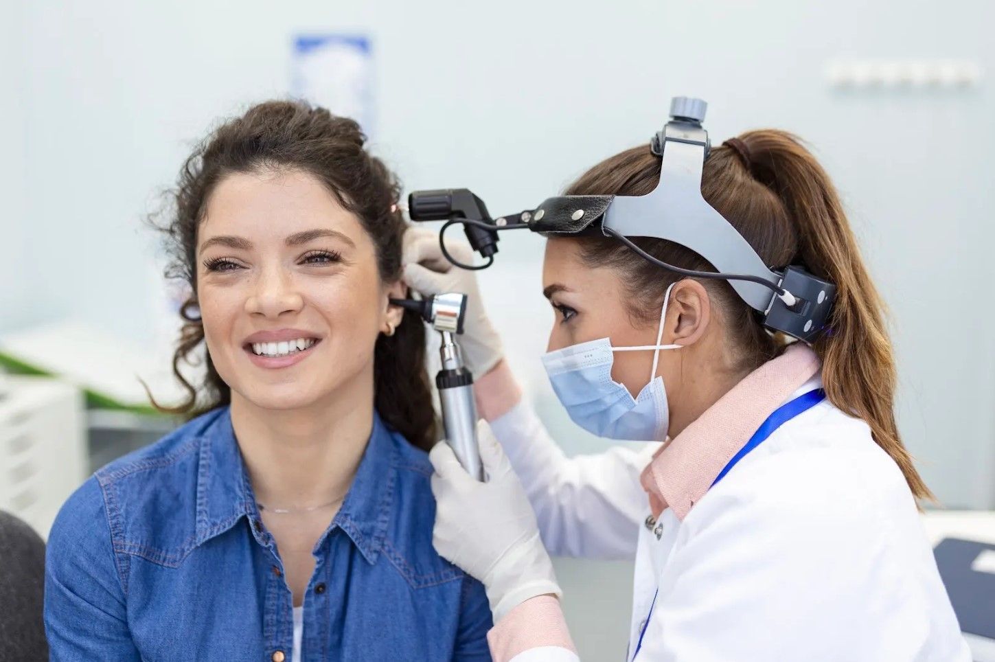 Clinician examines a patient’s ear with an otoscope in a bright medical office.