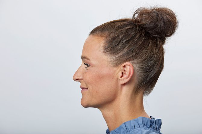 Smiling woman in a white sweater against a blue background, touching her ear