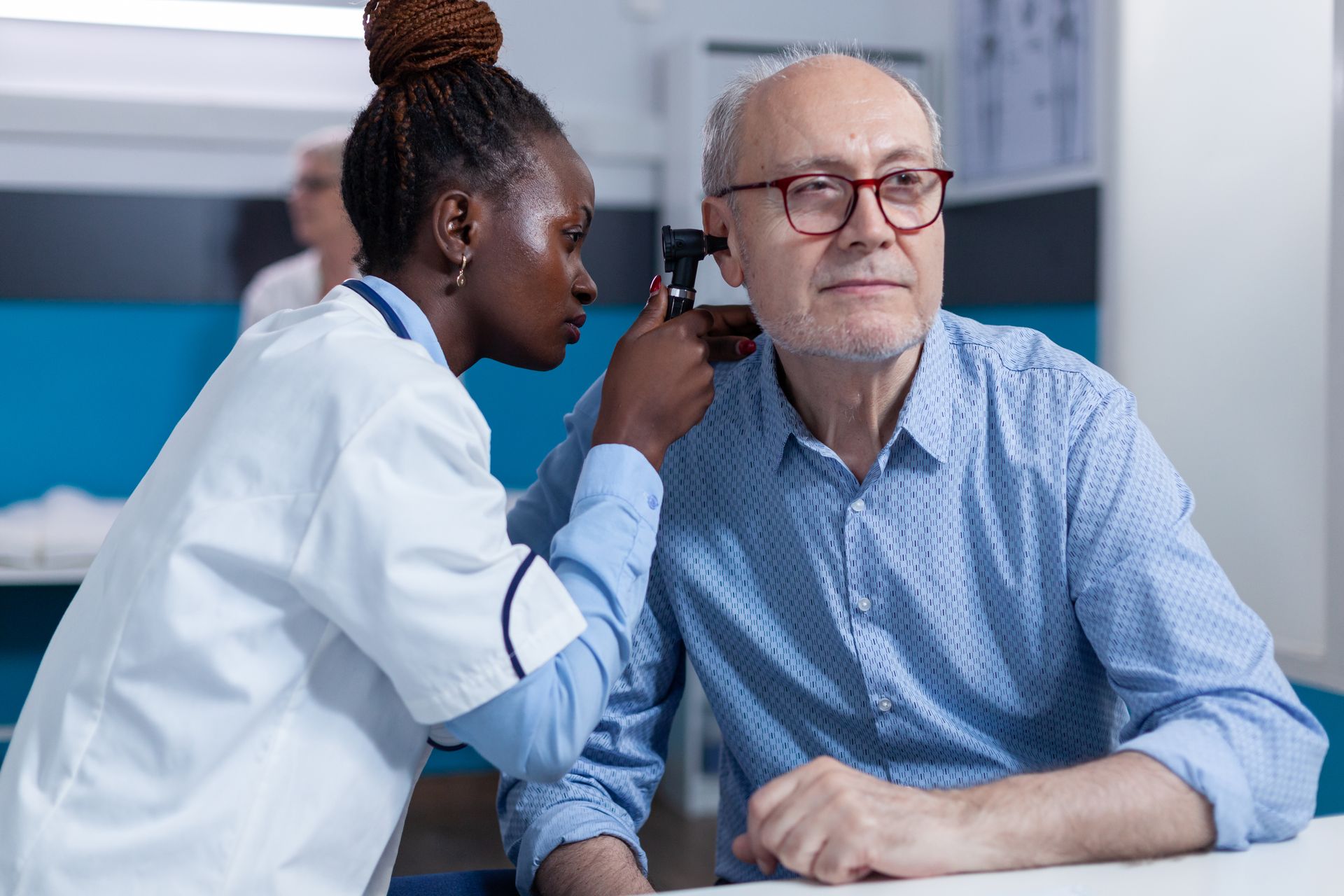 Clinician examining an older patient’s ear with an otoscope in a medical office