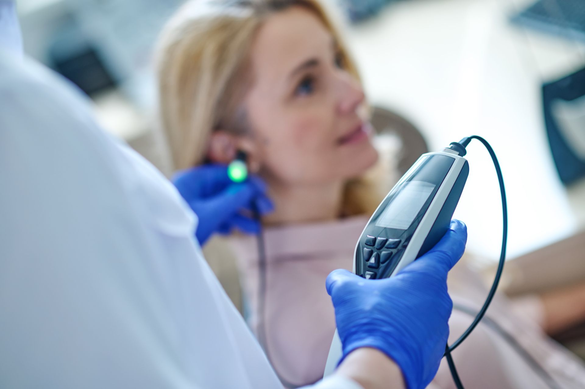 Clinician in blue gloves using a handheld medical device near a patient in a clinical setting