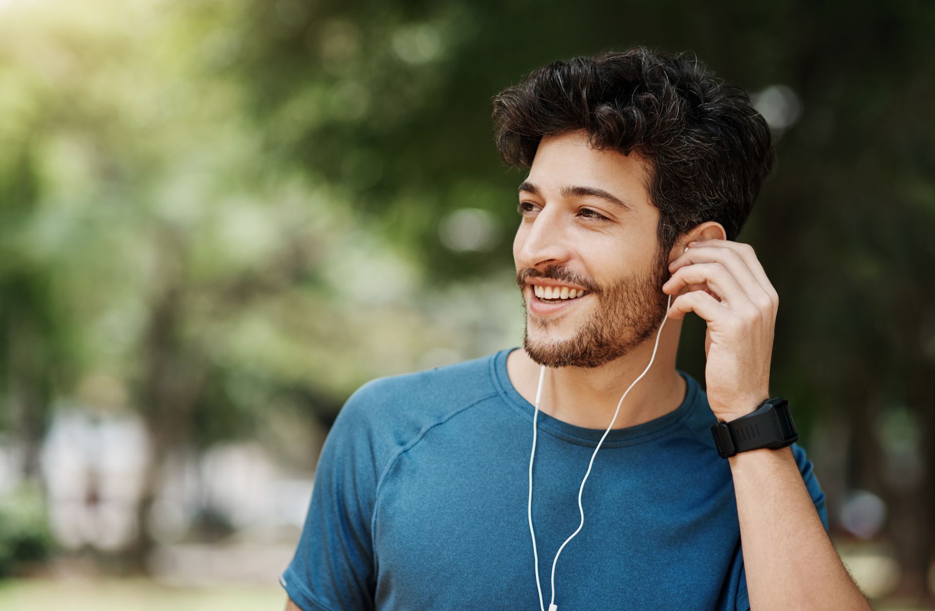 Smiling man in a blue shirt listening to earphones outdoors