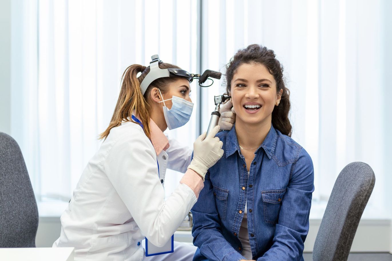 Audiologist examining a smiling patient’s ear in a bright clinic