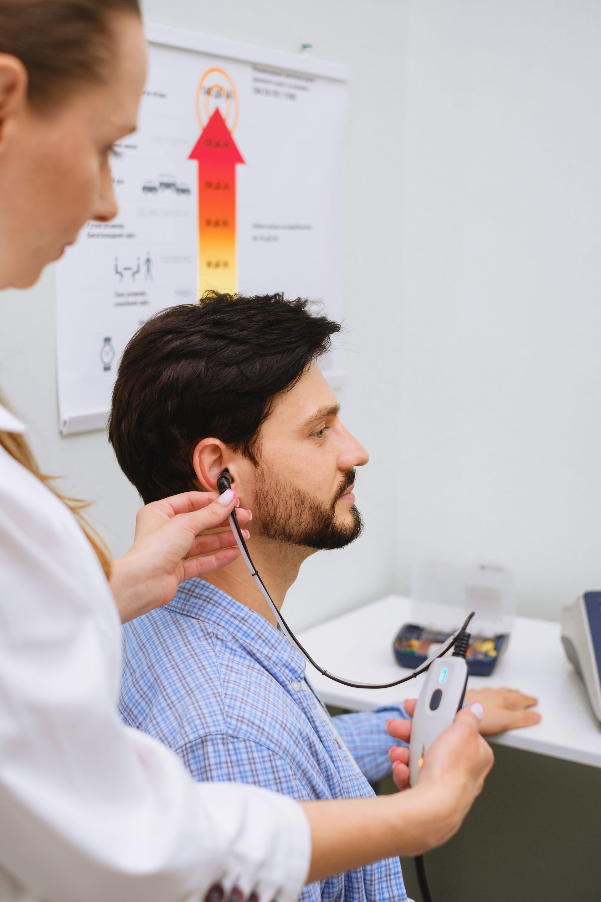 Healthcare worker adjusting earbuds on seated patient in a clinic, with medical chart in the background