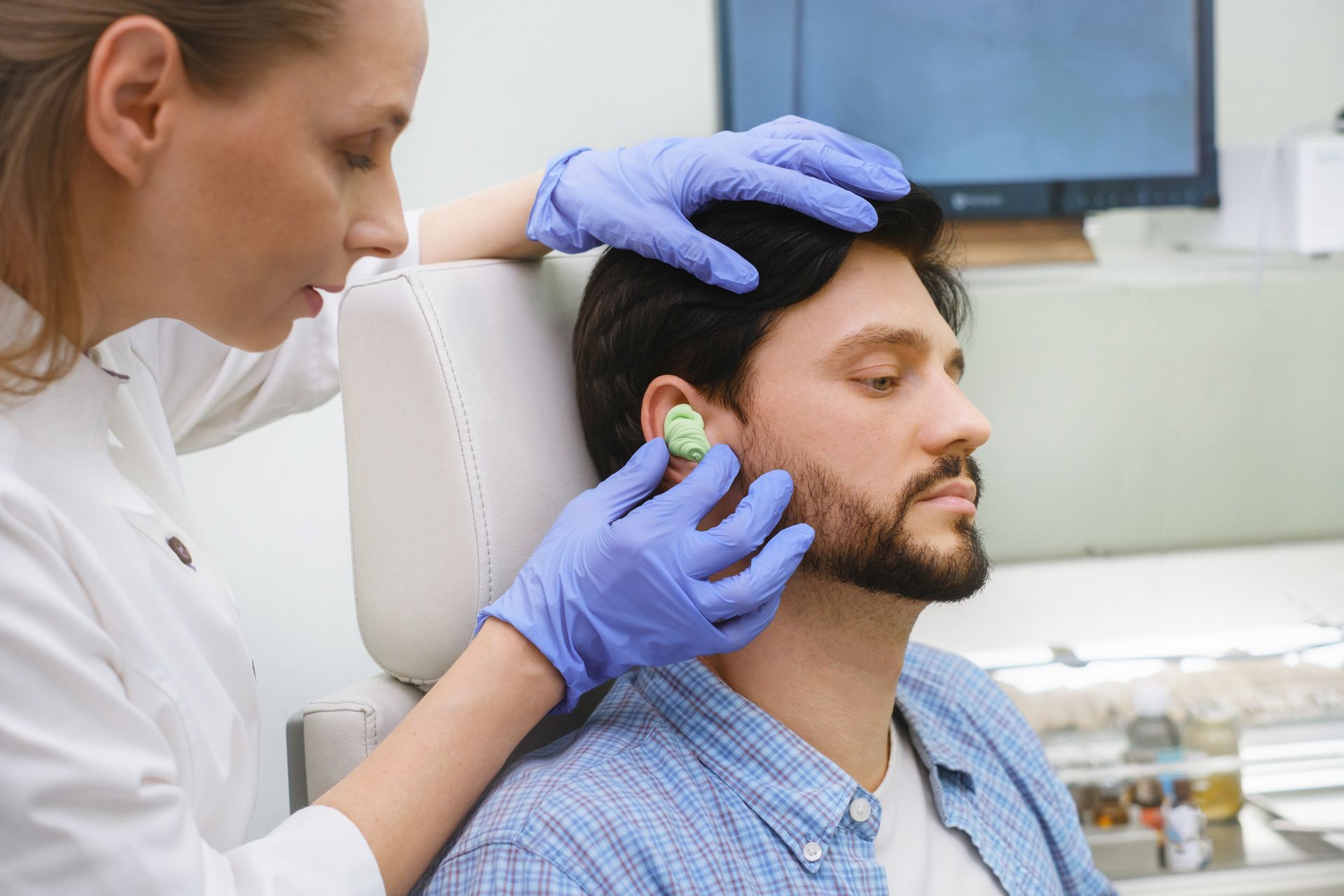 Clinician examining a man's ear with an otoscope in a medical office