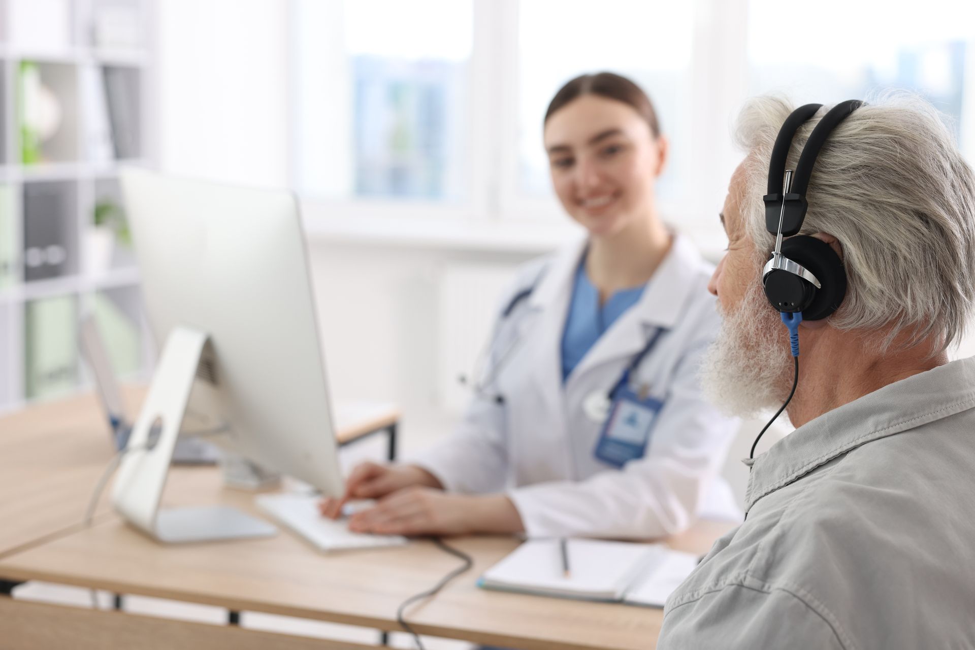 Telehealth consultation with doctor and patient wearing headphones at a desk in a bright clinic