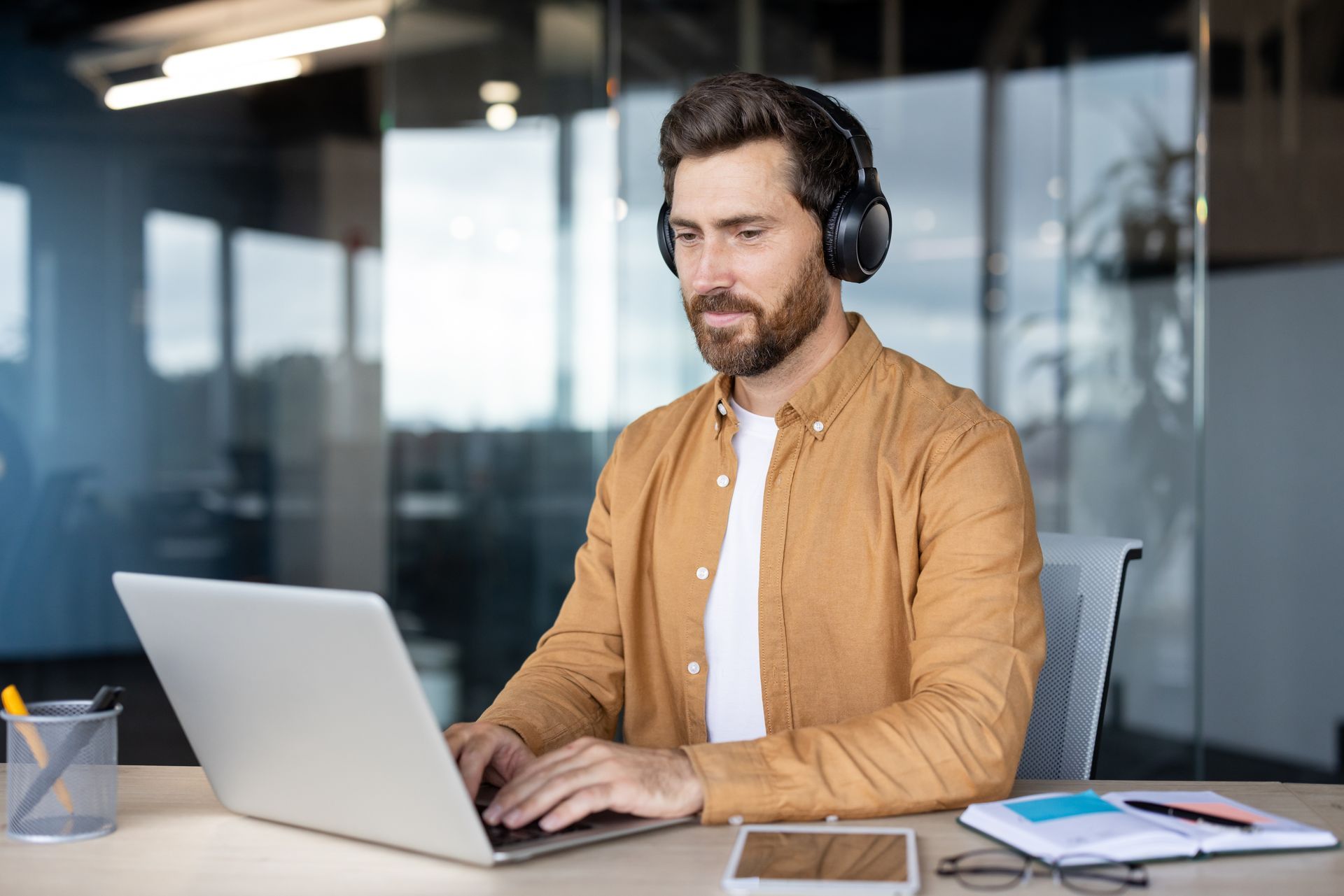 Man wearing headphones working on a laptop at a desk in a modern office