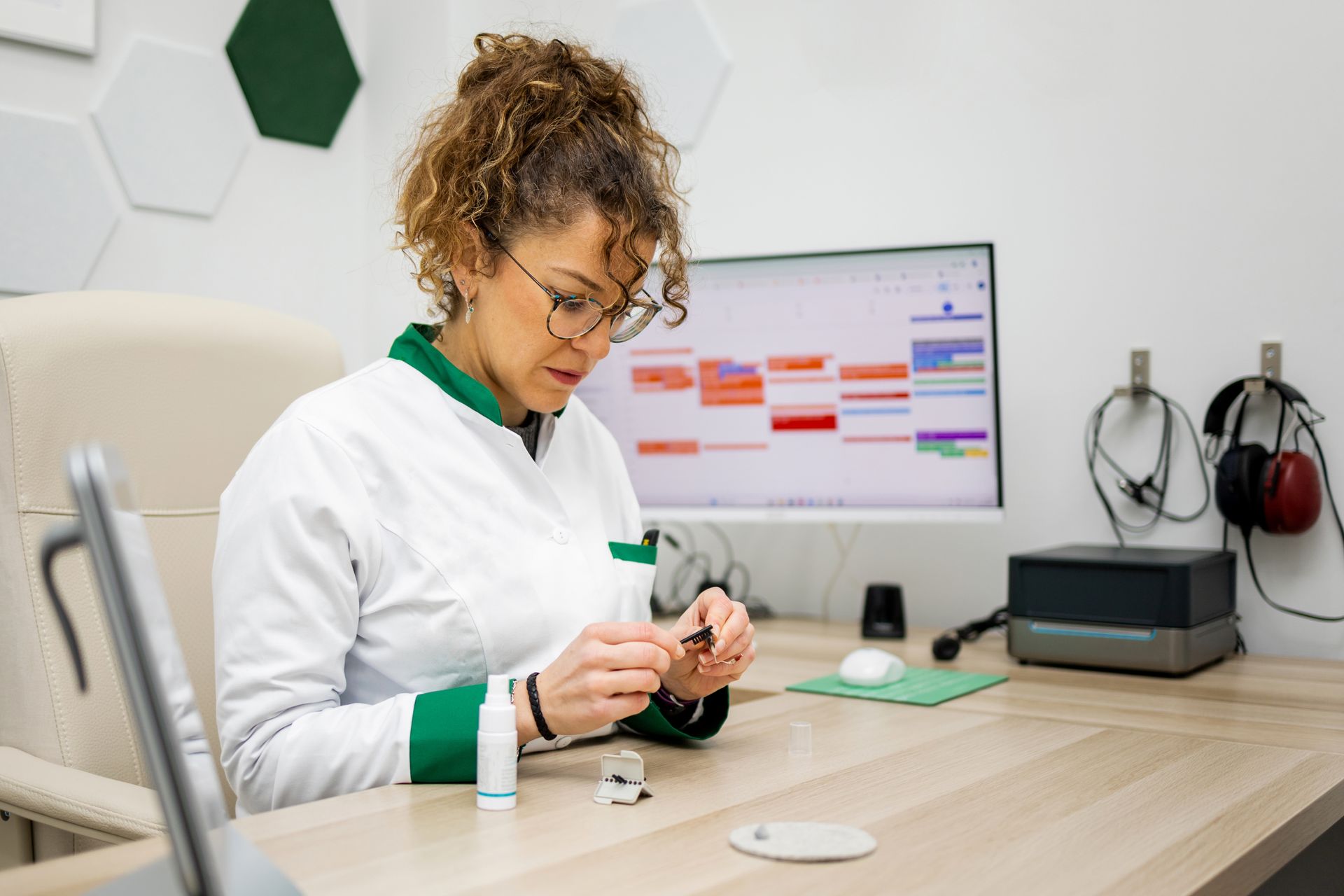 Lab technician examining a small sample at a desk with a computer monitor displaying data in the background