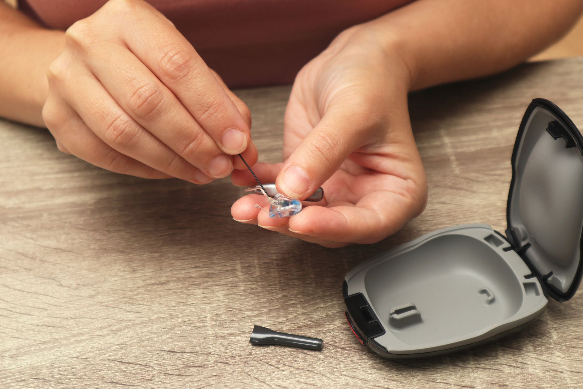 Hands using a screwdriver to fix a small hearing aid beside an open case on a table