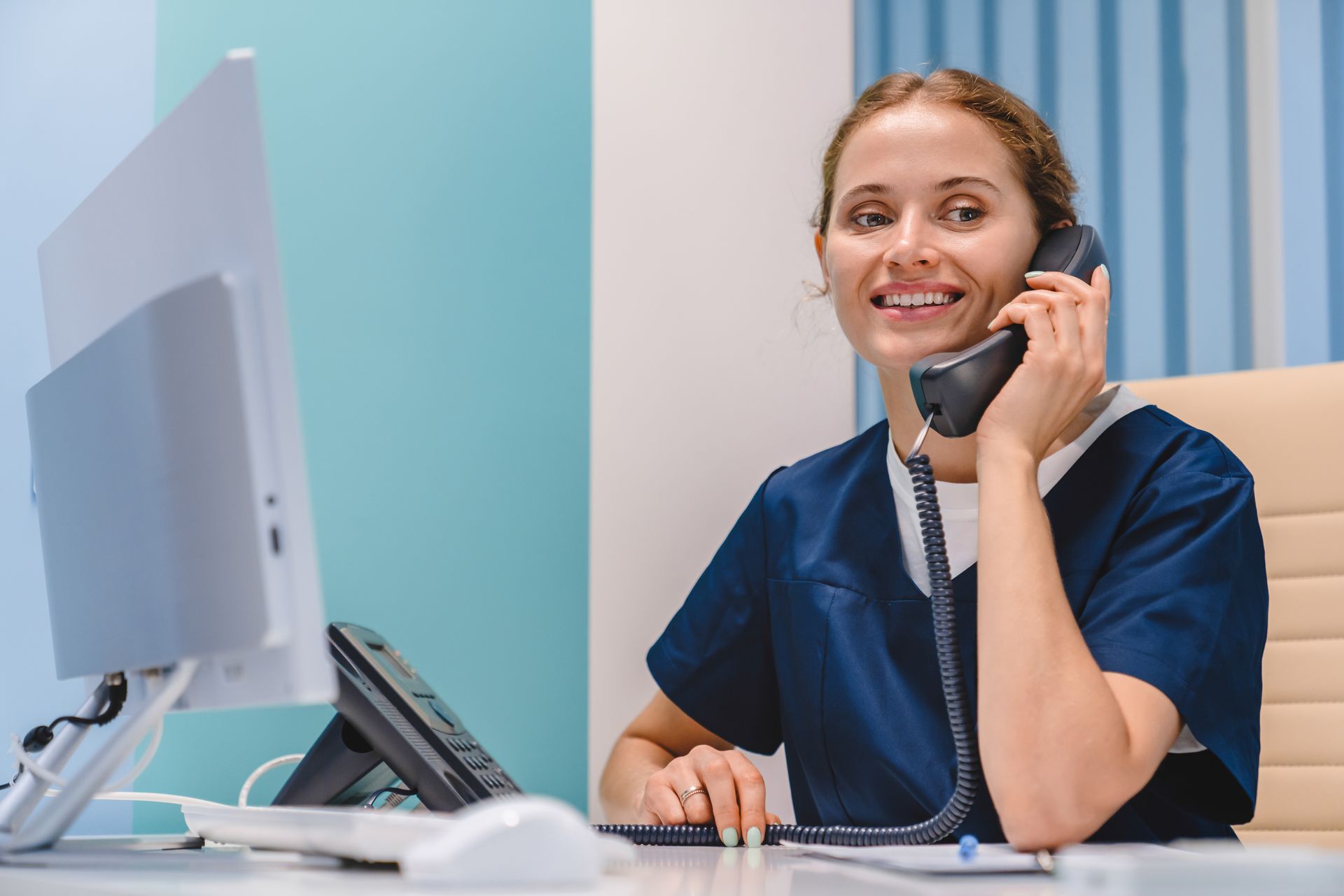 Smiling customer service agent in blue uniform talking on a phone at a desk with a computer